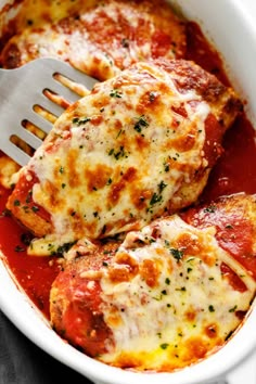 two pieces of chicken parmesan in a white casserole dish with a fork