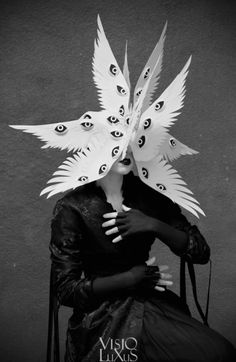 a woman sitting in a chair with paper wings on her head and hands over her face