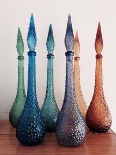 five different colored vases sitting on top of a wooden table