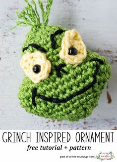 a crocheted green frog ornament hanging on a white wooden wall with black eyes