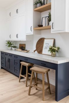 a kitchen with white cabinets and wooden stools next to a counter top that has plants on it