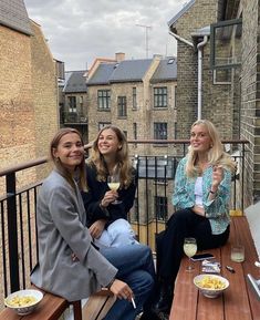 three women sitting at a table with food and drinks on the outside deck overlooking brick buildings