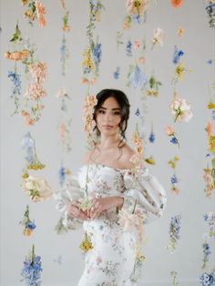 a woman standing in front of a wall with flowers hanging from it's sides