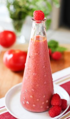 raspberry smoothie in a glass bottle on a plate with fresh raspberries