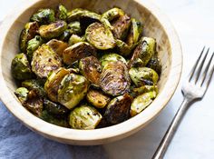 a bowl filled with brussel sprouts next to a fork and knife