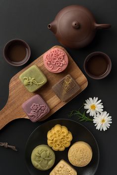 some cookies are on a black plate next to two cups and a teapot with flowers