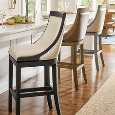 a kitchen with white counter tops and wooden chairs in front of a bar stool that has two wine glasses on it