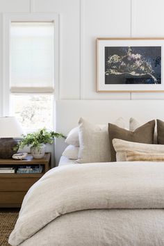 a bed with white linens and pillows in a bedroom next to a painting on the wall