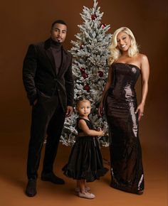 a man, woman and child standing in front of a christmas tree