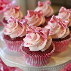 cupcakes with white frosting and pink bows are on a cake platter