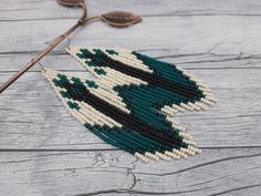 a pair of beaded earrings sitting on top of a wooden table next to a knitting needle