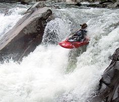 a man riding a red kayak on top of a river next to large rocks