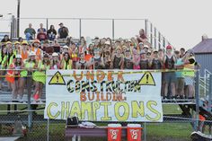 a group of people standing on top of a field holding up a sign that says under construction, build champions