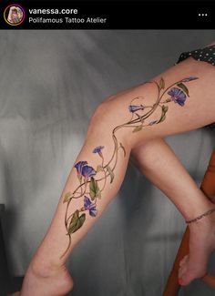 a woman's legs with tattoos on them and purple flowers painted on the leg