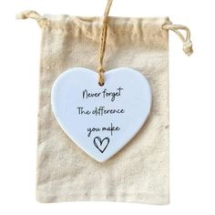 a white heart hanging from a string on top of a cloth bag with the words never forget