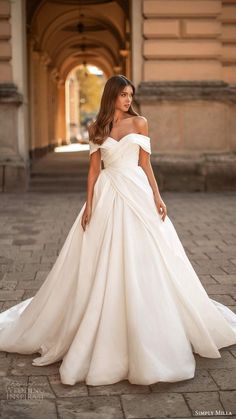 a woman in a white wedding dress standing on a brick walkway with an archway behind her