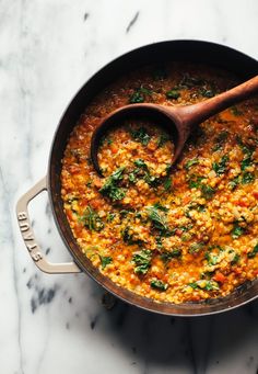 a large pot filled with food on top of a white marble countertop next to a wooden spoon