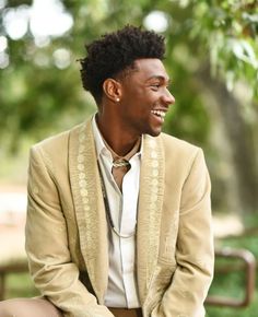 a man in a tan suit and white shirt is sitting on a bench smiling at the camera