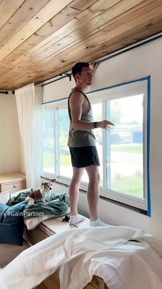 a woman standing on top of a bed next to a window