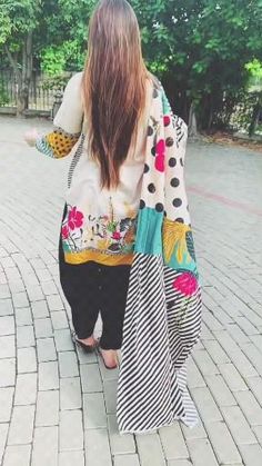 a woman with long hair walking down a brick walkway wearing a colorful jacket and black pants