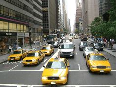 a city street filled with lots of yellow cabs and people walking on the sidewalk