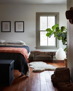 a bedroom with a bed, window and rugs on the wooden floor in front of it