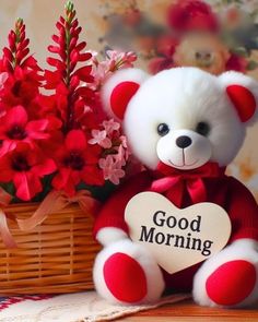 a white teddy bear sitting next to a basket with red flowers and a sign that says good morning