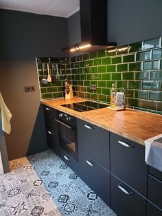 a kitchen with black cabinets and green tile backsplash, counter tops and drawers