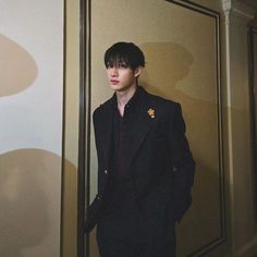 a man standing in front of a wall wearing a black suit and gold brooch