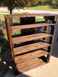 a wooden shelf sitting on the side of a sidewalk next to a tree and grass