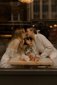 two women sitting at a table kissing each other