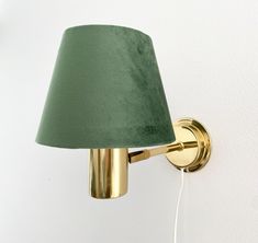 a green lampshade on the wall next to a white wall with a light plugged into it