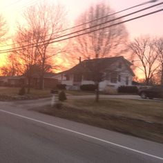 the sun is setting over some houses and cars on the street in front of them