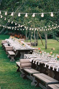 a long table is set up with place settings and lights strung from the trees in the background