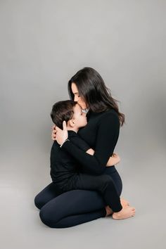 a mother and son hug while sitting on the floor in front of a gray background