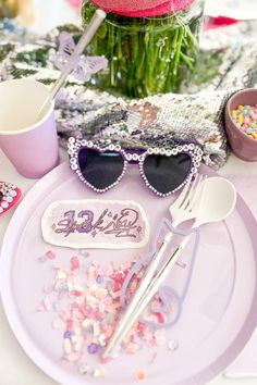 the table is set with pink and purple decorations, sunglasses, confetti, and flowers