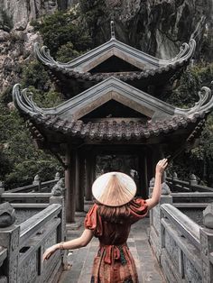 a woman wearing a hat and dress walking across a bridge