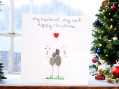 a christmas card with two rocks in the shape of a heart on it, next to a decorated christmas tree