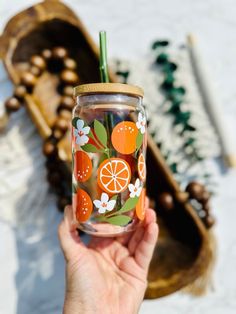 a hand holding a glass with oranges and flowers painted on it, next to other items