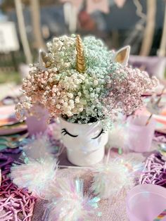 a table topped with a white vase filled with flowers and a unicorn face on top of it