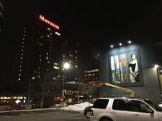 a white suv parked in front of a tall building at night with lights on it