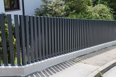 a metal fence on the side of a road next to some trees and bushes in front of a house