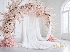 an arch covered in white fabric and pink flowers