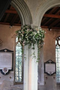 a tall white pillar with flowers hanging from it's sides in front of two windows