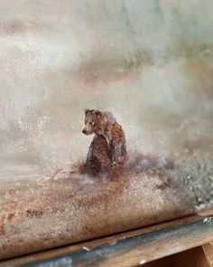 a small brown bear sitting on top of a wooden floor next to a painting easel