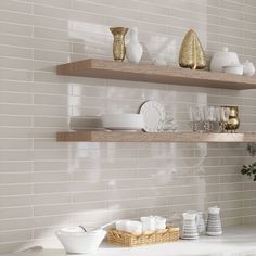 the shelves in this kitchen are filled with white dishes and gold vases on them