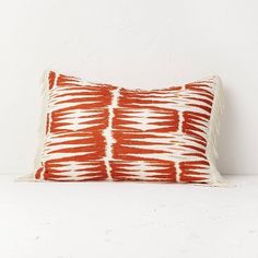 an orange and white pillow sitting on top of a bed in front of a wall