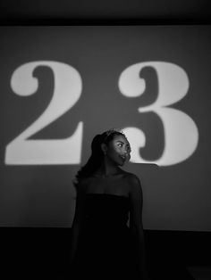 a woman standing in front of a large number on a wall with the numbers 23 and 28 projected behind her