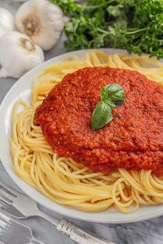 a white plate topped with spaghetti and sauce next to garlic, parsley and pepper