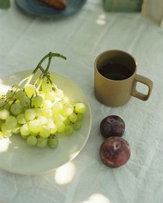 grapes and plums on a plate next to a cup of coffee